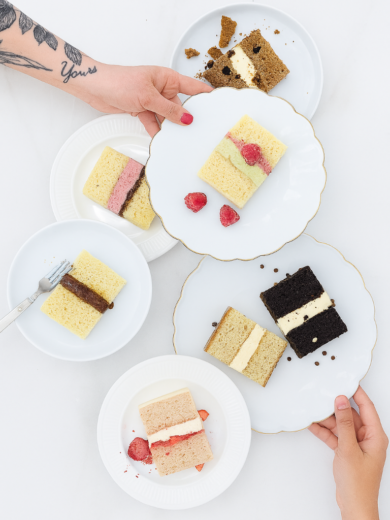Small cakes on white plates with hands reaching for them on a light background